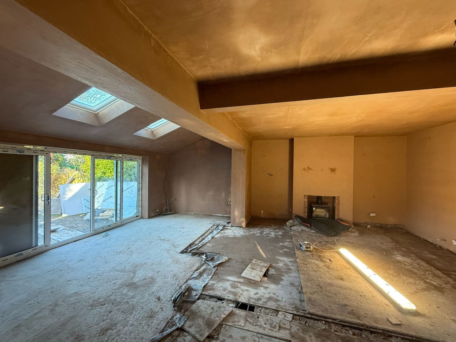 Open-plan UK extension interior freshly bonded and skimmed by MCB — walls, ceilings and structural beams finished smooth with pink plaster, bi-fold doors and roof lanterns in place