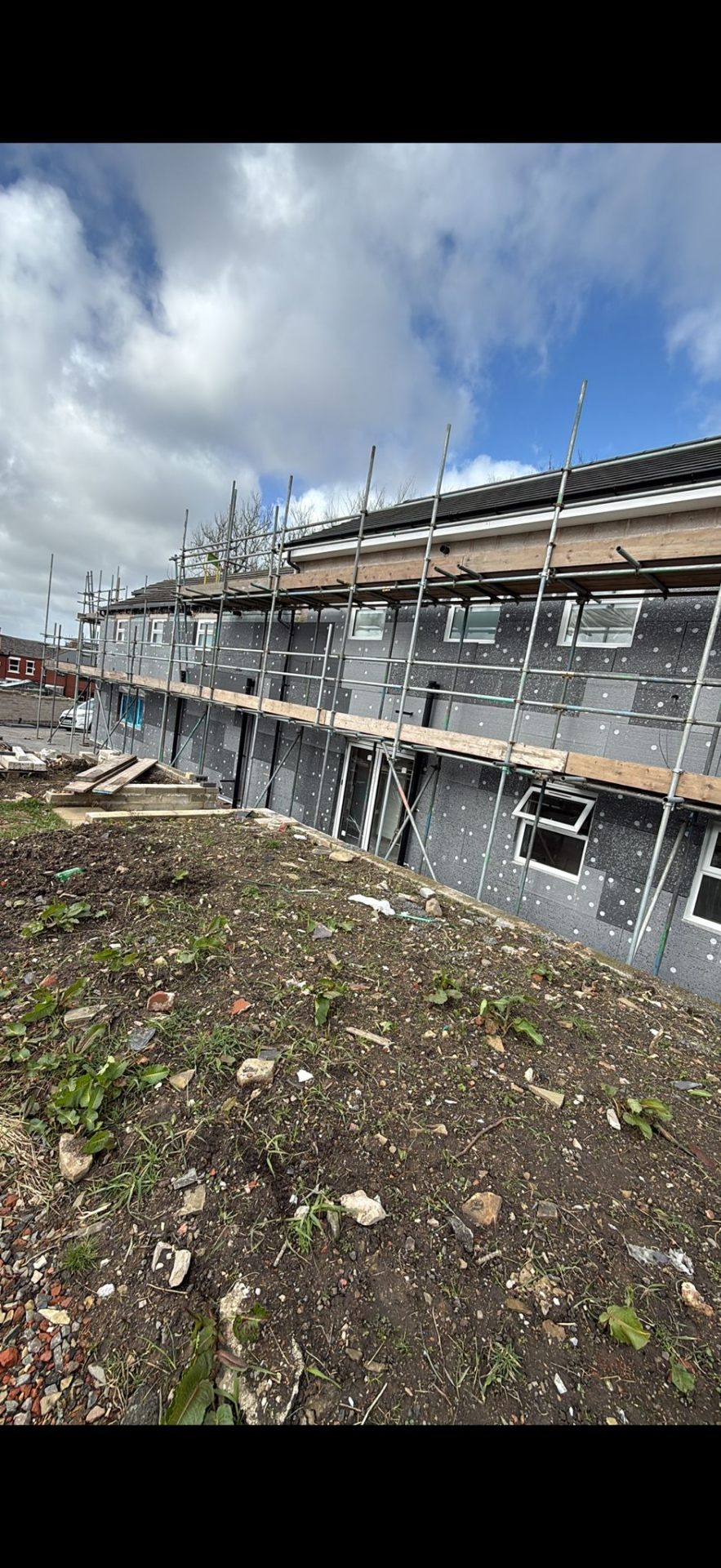 External Wall Insulation system mid-installation on a UK property — grey EPS insulation boards fixed and mechanically pinned across the elevation, scaffold in place ready for base coat and render